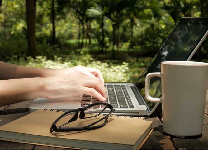 Hands typing at a keyboard with a forest behind.