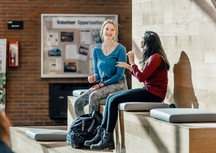 Two young girls with backpacks talking in the hall.