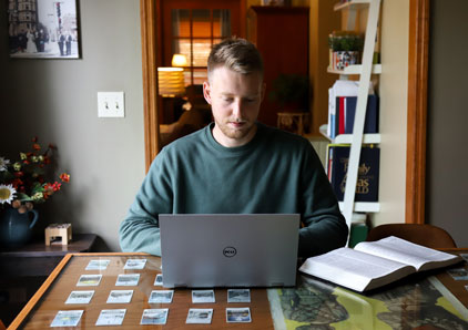 Male student sits at kitchen table with book and laptop.