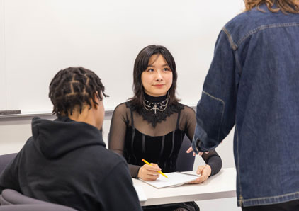 Student seated talking with teacher.